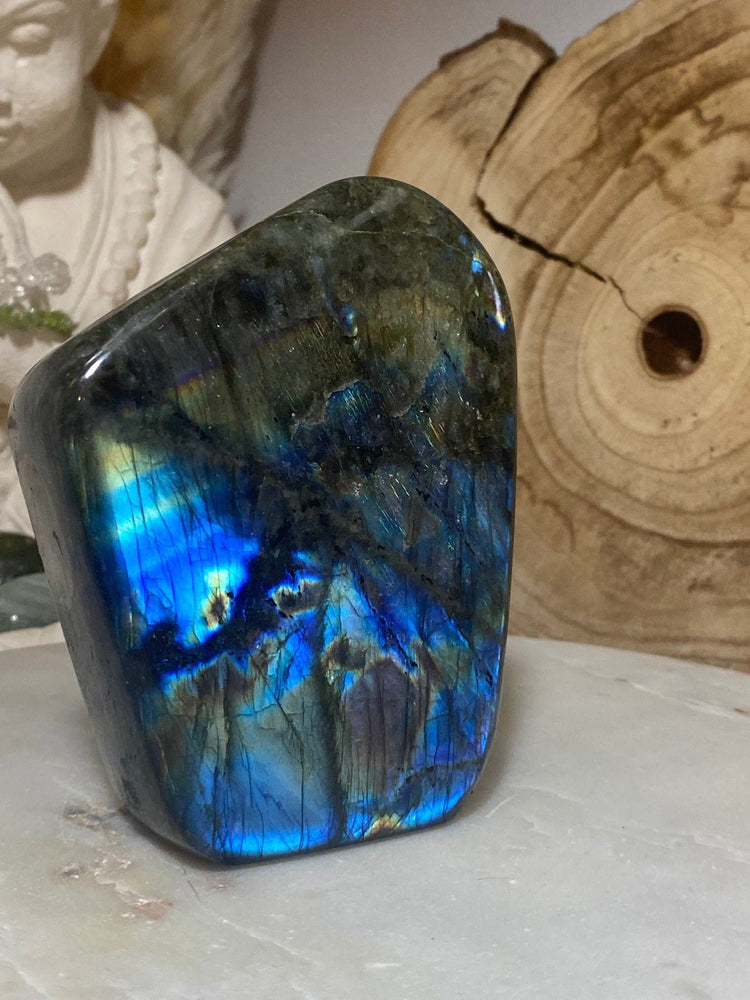 Labradorit - Heilsteine mit besonderer Wirkung. Labradorit-Stein auf Marmorplatte mit Holz im Hintergrund.