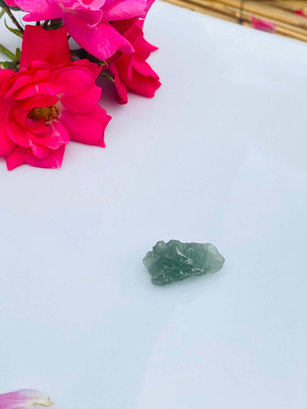 Ein Stück grüner MOLDAVIT auf weißem Porzellan.