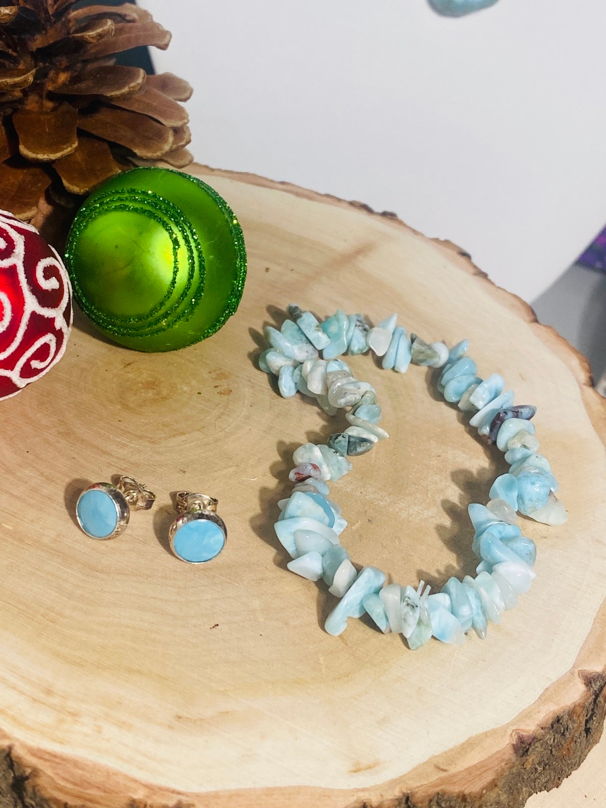 Ein Paar Larimar Ohrstecker mit Splitterarmband auf einem Holzbrett mit Weihnachtsedeko.